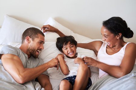 Happy, playing and parents with child in bedroom for bonding, love and playful relationship. Family, childhood and mother, father and kid tickle for laughing, fun or relax on bed together in homeの写真素材