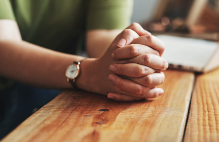 Woman, hands and praying on desk for worship, jesus christ and christian praise for salvation in home. Female person, spiritual healing and thank you to God, practice religion and grace for peaceの写真素材