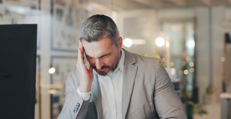 Stress, headache and mature man at desk with computer, night work and frustrated with time management. Late, fatigue and tired businessman in office with burnout, anxiety and online deadline pressureの写真素材