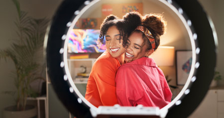 Happy women, influencer and hug with ring light for video recording, vlogging or content creation at home. Young, female person or friends in vlog for online trend, beauty or makeup tips togetherの写真素材