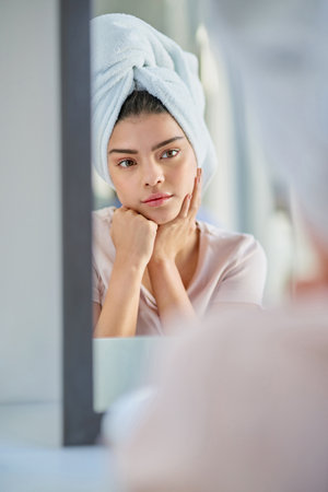 Mirror, thinking or woman in bathroom with beauty, glow or wellness in home for treatment. Towel, serious and girl with confidence, cosmetics results or skincare ideas with health or morning routineの写真素材