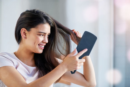 Woman, grooming and brushing hair in home, texture and morning for getting ready in bathroom. Female person, cosmetics tool and hairbrush for hairstyle, cleaning and treatment for healthy growthの写真素材