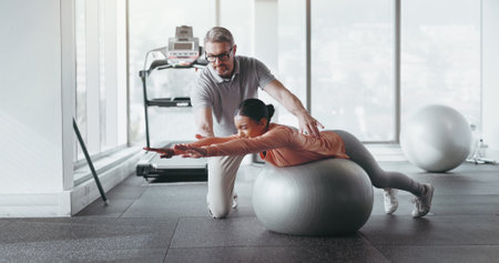 Ball, woman and personal trainer in gym for fitness, rehabilitation or stability training. Man instructor, girl or physiotherapy in yoga center for core strength, pilates practice or help in exerciseの写真素材