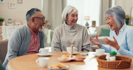 Laugh, tea and senior friends at table for funny conversation, snacks and retirement together in house. Group, party and man speaking with elderly women smile for breakfast, communication and bondingの写真素材