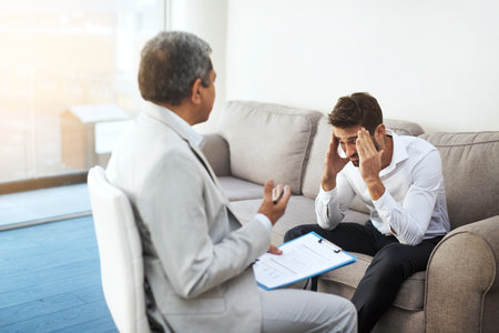 Men, doctor and patient at office with headache on consultation, checkup and examination. People, healthcare and discussion with document for migraine symptoms, sickness and diagnosis at clinicの写真素材