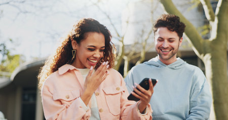 Phone, laughing and couple outdoor on date, travel or reading funny meme in city together. Mobile, happy man or interracial woman at park on app online for joke, watch video or comedy on social mediaの写真素材