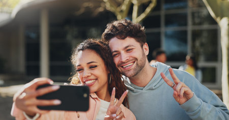 Happy couple, students and selfie with peace sign at campus for photography, picture or memory. Young, man and woman with smile, emoji or gesture for moment, capture or friendship at universityの写真素材