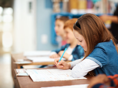 School, kids and girl in classroom with writing for growth, child development and notebook for education. Study, learning and students with notes for knowledge, exam and children thinking at deskの写真素材