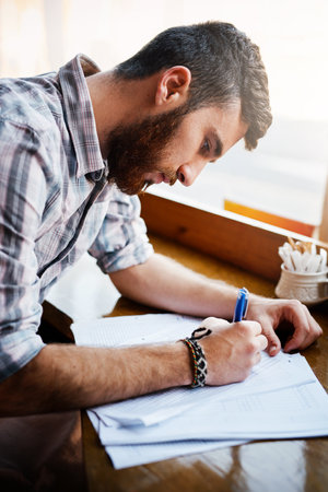 Business, man and writing with documents at cafe for finance planning, vendor contract and inventory budget. Male person, paperwork and customer feedback form, sales profit and reading informationの写真素材