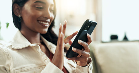 Indian woman, phone and text in home with social media, website scroll and internet meme in living room. Tech, smile and couch with typing, relax and online app with post and digital chat on mobileの写真素材