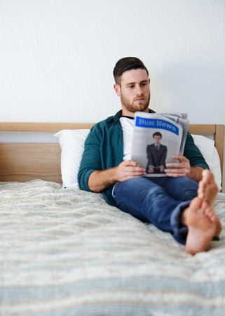 Man, relax and newspaper in home for reading, business update and social knowledge in bed. Person, chill and article in press for corporate news, stock market information and job search in bedroomの写真素材