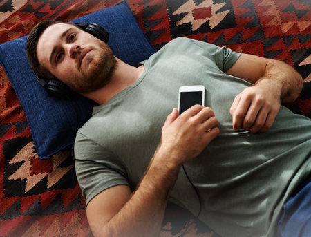 Man, headphones and music with phone and online streaming on living room floor to relax. Weekend,...