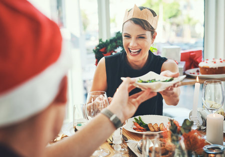 Christmas, food and laugh with people at dining table for festive celebration, decoration or winter holiday. Social, merry season and xmas eve with friends at home for support, vacation or traditionの写真素材