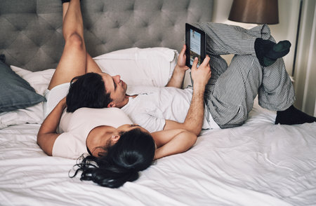 Couple, relax and research tablet on bed for travel destination, holiday location and scroll vacation website. Love, people and resting in bedroom with digital app for bonding, relationship and careの写真素材