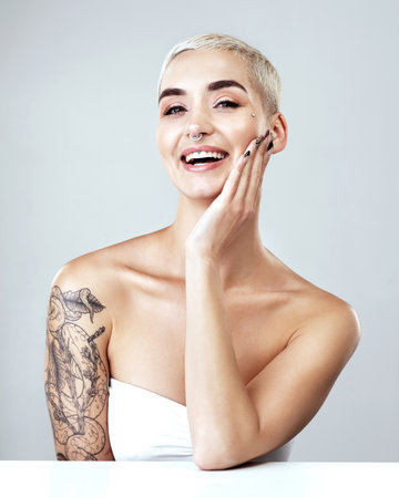 Woman, portrait and smile with skincare in studio for natural beauty, results and facial glow. Person, tattoo and piercings with confidence for dermatology, cosmetics and makeup on white backgroundの写真素材