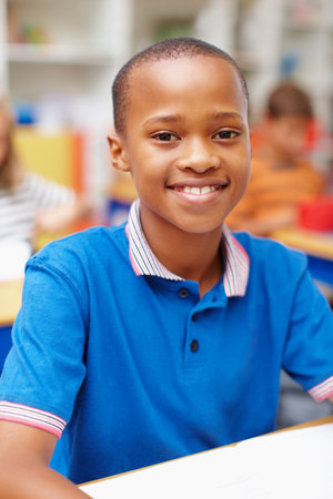 Smile, portrait and boy in classroom for education, growth and child development at elementary school. Happy, face and student at desk for learning, study and future opportunity for scholarship.の写真素材