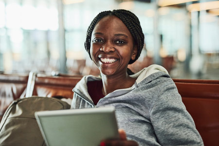 Portrait, black woman and tablet in lobby at airport for social media, browsing internet and flight schedule. Girl, smile and digital in waiting room for departure update, streaming and entertainmentの写真素材