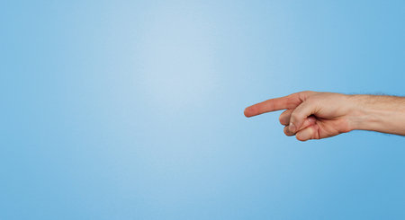 Finger, point and arm of person in studio for information, direction and announcement of news. Hand, gesture and emoji by mockup space for review, answer and feedback of opinion on blue backgroundの写真素材