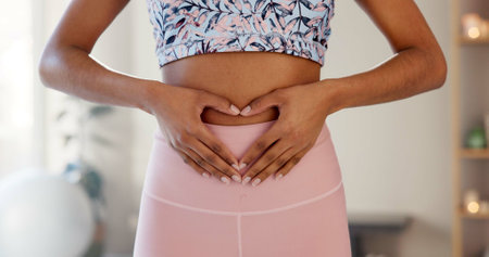 Woman, heart and hands on stomach for fitness, wellness or body care in home. Love, abdomen or girl with sign for digestion, gut health and show progress of keto diet or detox for weight loss resultsの写真素材