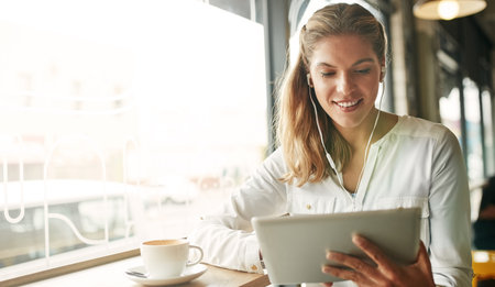 Woman, tablet and coffee shop for listening to music, earphones and website for streaming radio. Female person, restaurant and surfing social media on internet, relax and cup of espresso for podcastの写真素材