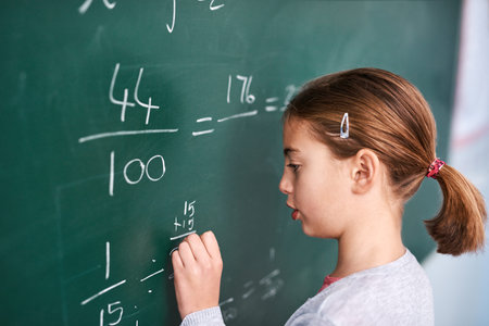 Girl, writing and math with chalkboard for equation, education or learning in classroom at school. Female person, child or young kid with fraction, numbers or problem solving for answer or solutionの写真素材
