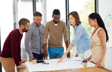 Architecture, business people or meeting with blueprint in office for planning home remodeling project. Collaboration, architect team or pointing to floor plan for building design, draft or diversityの写真素材