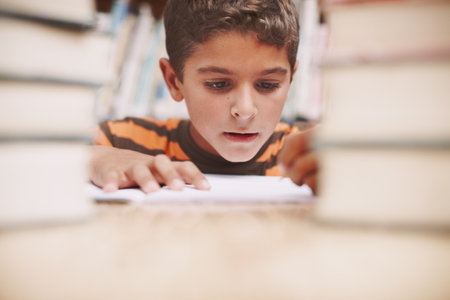 Child, writing and study in library for education, knowledge and solution for development at elementary school. Young boy, learning and books on table for lesson, growth and progress in assessmentの写真素材