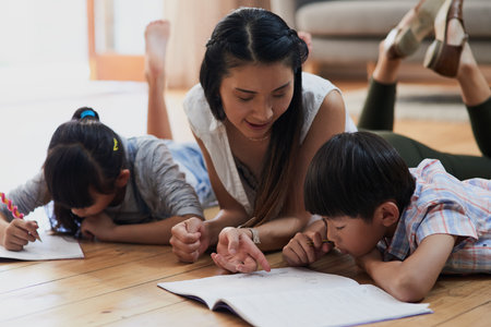 Asian mother, children and homework on floor with art, color and happy with school project in living room. People, mom and kids with books, support and development for scholarship in family houseの写真素材