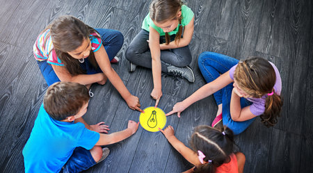 Children, pointing and playing a game on floor with lightbulb, decision making and learning. Diversity circle, people and problem solving with educational activity, solution and knowledge on top viewの写真素材