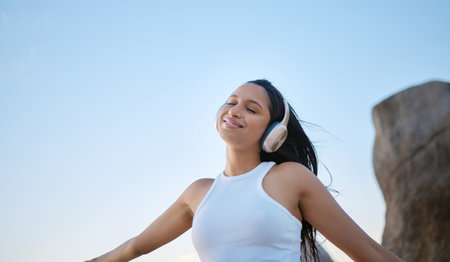 Outdoor, woman and happy with eyes closed on headphones for music, audio and radio in Brazil. Female person, outside and smile or satisfied with streaming for motivational sound to relax on breakの写真素材