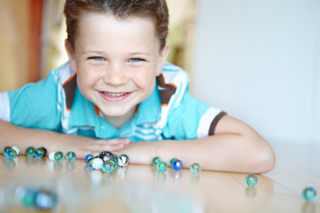 Floor, boy and smile with playing marbles on portrait for fun on school break at home in Scotland. Male person, kid and happy at apartment with toys for games, child growth and brain developmentの写真素材