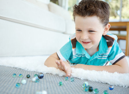 Happy, kid and play with marble in home for funny game and relax in living room. Smile, child and boy with glass balls or toys on carpet for creative collection, laughing and development on floorの写真素材
