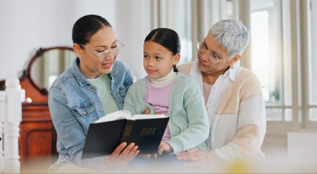 Grandmother, child and mother with bible in home for generations, worship and learning religion. Family, women and little girl with scripture in house for gospel, teaching or education of Holy Spiritの写真素材