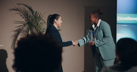 Business women, handshake and smile for prize, congratulations or meeting on event stage. Celebration, shaking hands and introduction for conference, award or interview for tradeshow presentationの写真素材