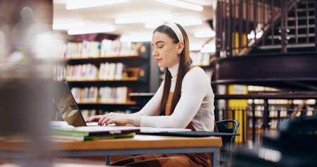 Education, laptop and research with woman in library for knowledge, learning and college thesis. Academy, future and university with student and online portal for exam, project and scholarshipの写真素材