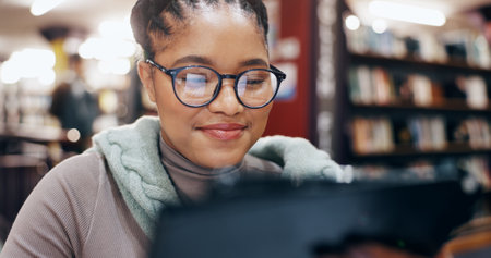 African, woman and smile with tablet in library for research information, university news and study schedule. Student, digital and reading online with education ebook, exam results and project reportの写真素材
