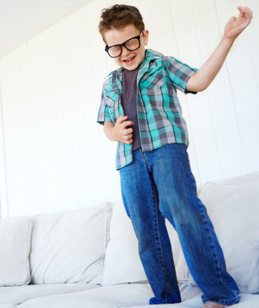 Dance, playing or kid with air guitar on sofa for comedy, humour or funny joke for rock and roll. Happy, excited or crazy boy child with music, celebration or imaginary instrument on couch in homeの写真素材