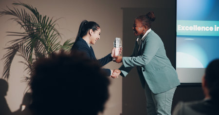 Handshake, award and smile of women, seminar and congratulations for success, event and corporate. Thank you, professional and celebration of hard work, winning and holding hands for conferenceの写真素材