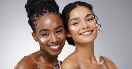 Portrait, cream and women with skincare, shine and dermatology on white studio background. Face, happy friends and people with lotion, aesthetic and grooming routine with cosmetics, glow and beautyの写真素材