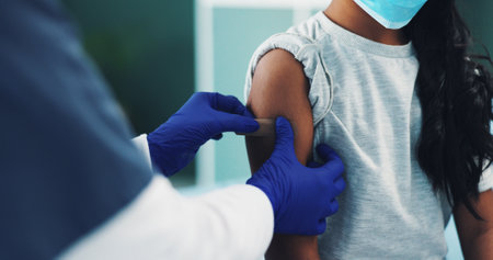 Hands, child and nurse with bandage for vaccine, safety and mpox prevention closeup in pediatric hospital. Girl, medical doctor and apply plaster on arm for protection, virus immunity and healthcareの写真素材