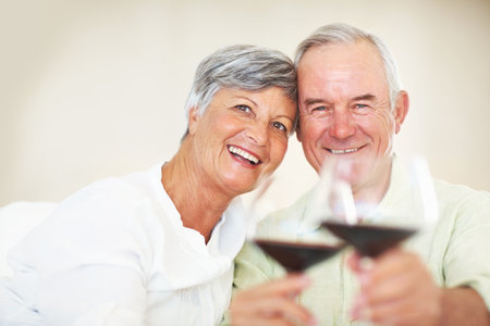 Happy, mature couple or cheers with red wine or glasses for toast, celebration or date together at home. Elderly, man and woman with smile, drink or beverage for holiday, bonding or romance at houseの写真素材