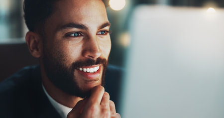Night, thinking and happy man in office with laptop, business plan or ideas for web project at digital agency. Research, overtime and businessman at desk reading email, report or good news with smileの写真素材