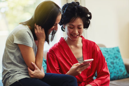 Phone, smile or wedding with bride and bridesmaid in home living room for communication or conversation. App, search or social media with woman friends in apartment together for preparation of vowsの写真素材