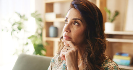 Mature, woman and thinking on couch with stress in home for financial crisis, recession news and worried. Person, thoughtful and reflection on sofa in lounge with debt anxiety and depression in houseの写真素材