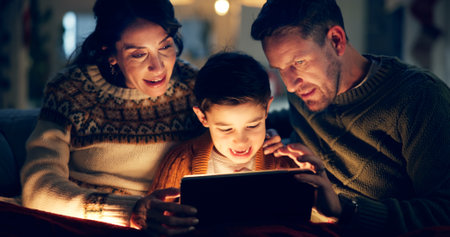 Tablet, relax and child with parents in home watching movie, film or show online for entertainment. Happy, light and kid on sofa with mother and father streaming video on digital technology at night.の写真素材