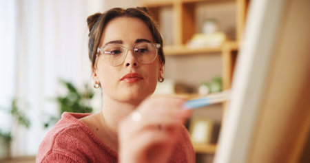 Artist, painting and woman with canvas in home for creative artwork, drawing and design with paintbrush. Hobby, art skill and person with easel in studio for inspiration, project and illustrationの写真素材