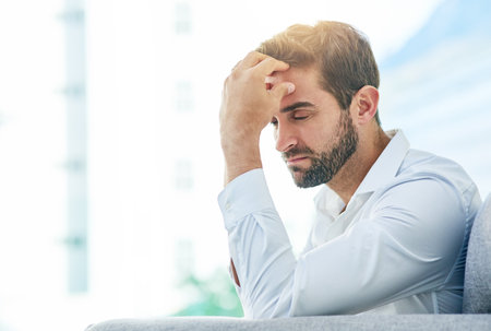 Businessman, headache and work stress in office, employee burnout and thinking on career crisis. Male person, tension migraine and professional on couch in workplace, mental health and frustratedの写真素材