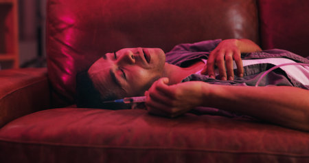 Drugs, overdose and man on couch with needle, health risk and narcotic danger in apartment at night....