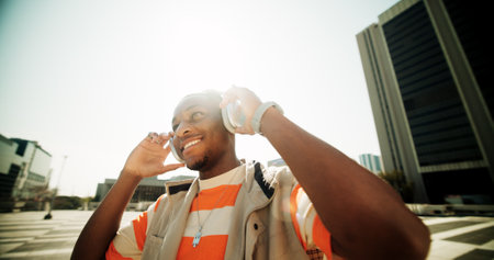 Music, headphones and streaming with black man in city for sound, playlist and techno. Hip hop, podcast and broadcast with gen z person listening in outdoor to audio for radio, happiness and summerの写真素材