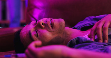 Drugs, overdose and man on couch in dark with needle, health risk and narcotic danger in apartment at night. Emergency, addiction and person on sofa with syringe, fentanyl crisis and blackout in homeの写真素材